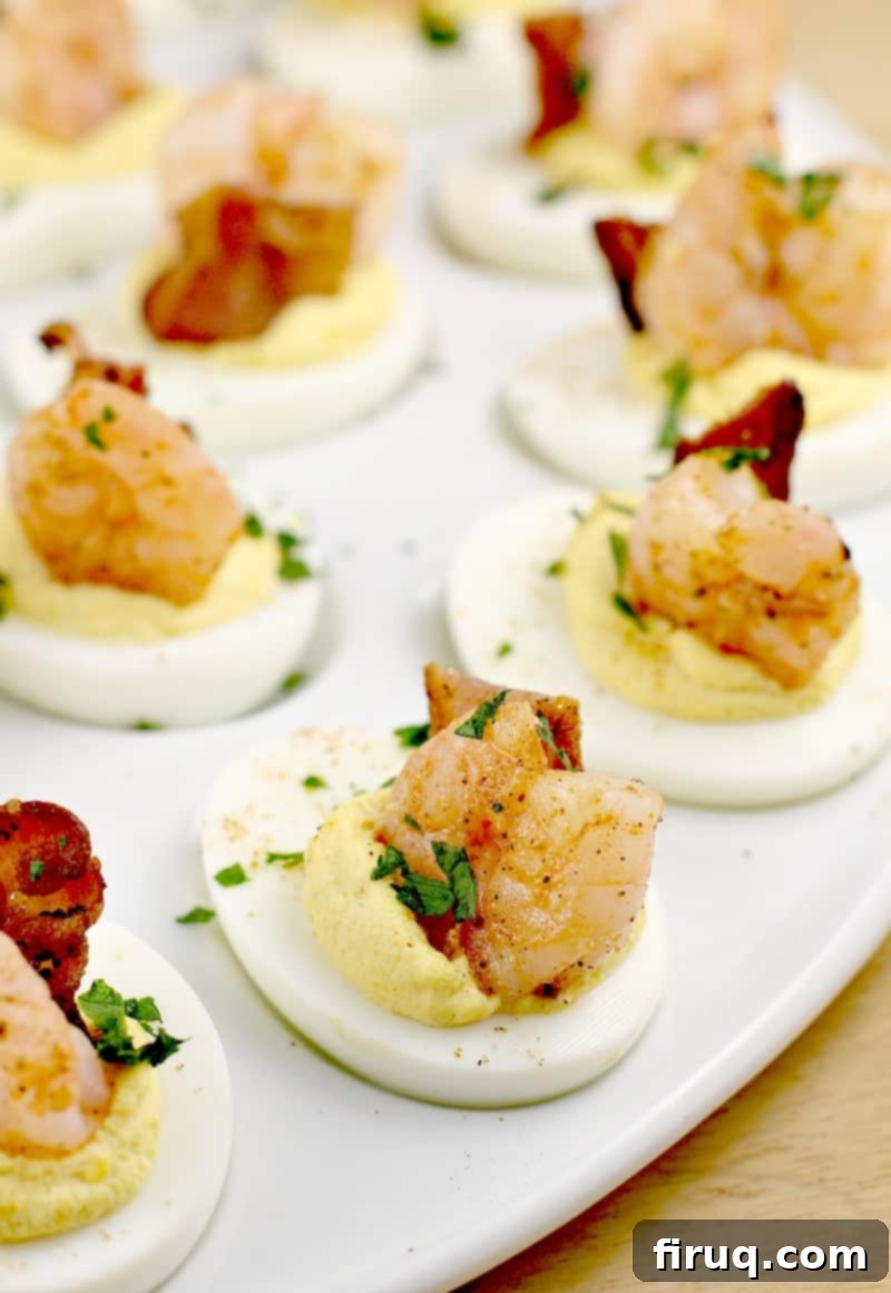 Zesty Creole Shrimp Deviled Eggs with Crispy Bacon 2 fully assembled shrimp deviled eggs on a white platter, garnished with fresh herbs and ready to serve
