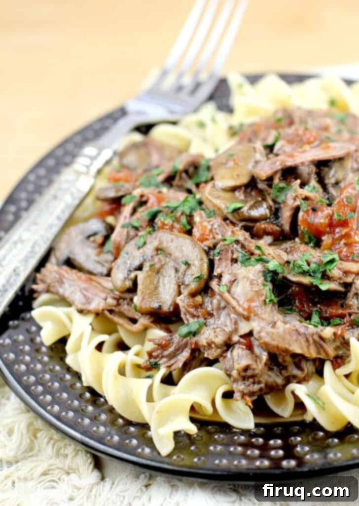 Zesty Cajun Instant Pot Pot Roast 2 side view from the left of the pot roast with beer over noodles on a plate with a fork, placed on a cutting board