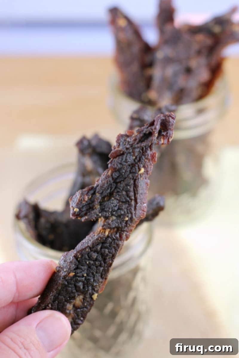 Homemade Beef Jerky Made Easy 12 hand holding a piece of jerky; mason jars filled with jerky in the background