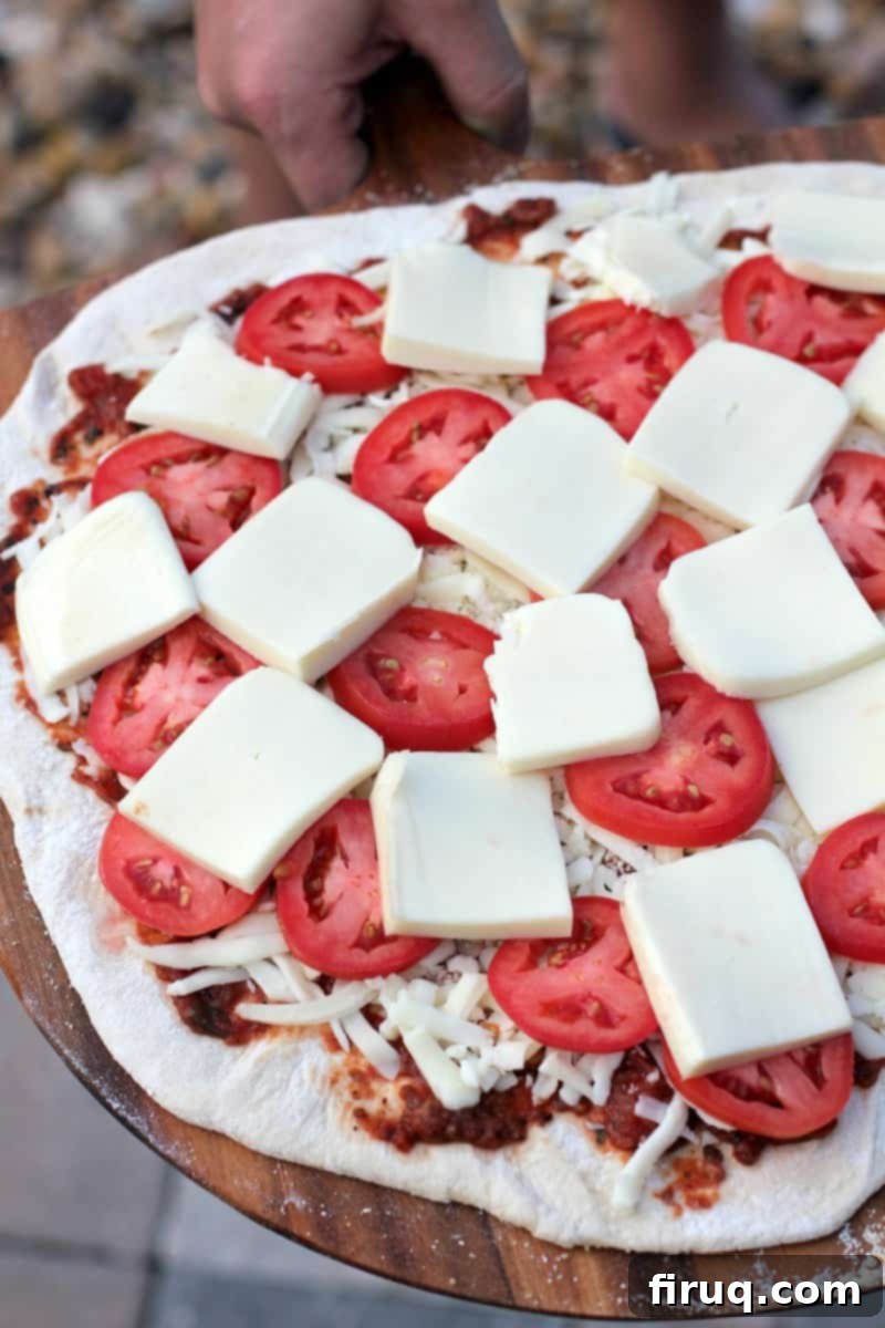 Perfect Pizza Margherita on the Big Green Egg 5 assembled pizza ready to cook topped with slices of tomato and cheese