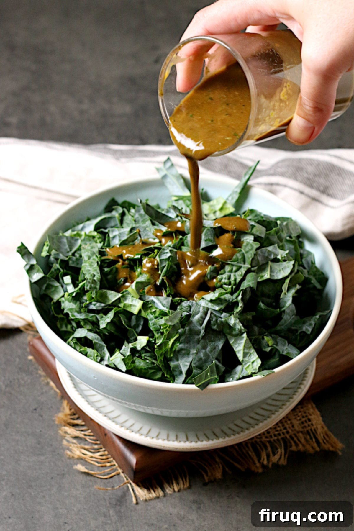 Dressing a Kale Salad with Vinaigrette A hand gracefully pouring the homemade Basil Balsamic Vinaigrette over a generous bowl of fresh shredded kale, ready for tossing and enjoyment.