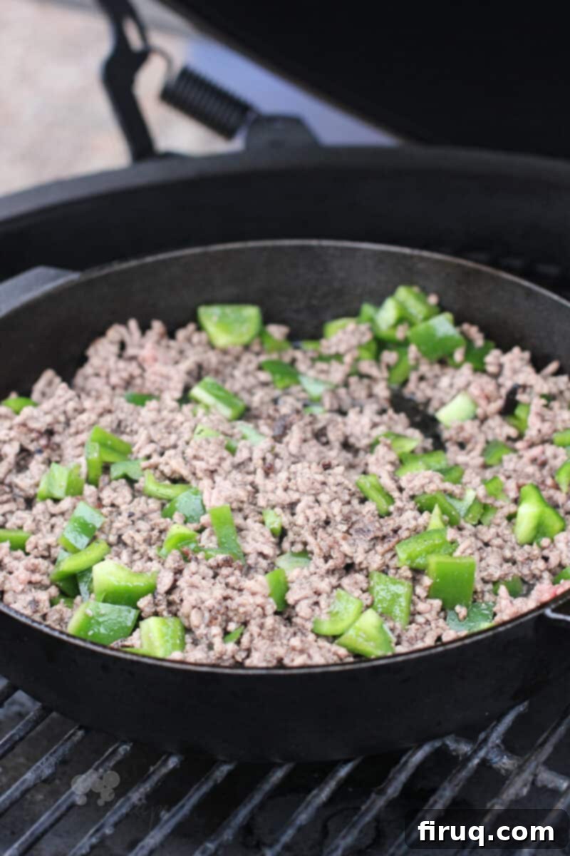 Grilled Beer-Infused Bacon Cheddar Joes 5 Cooked ground beef with green bell pepper in a cast iron pan on the grill, simmering with sauce