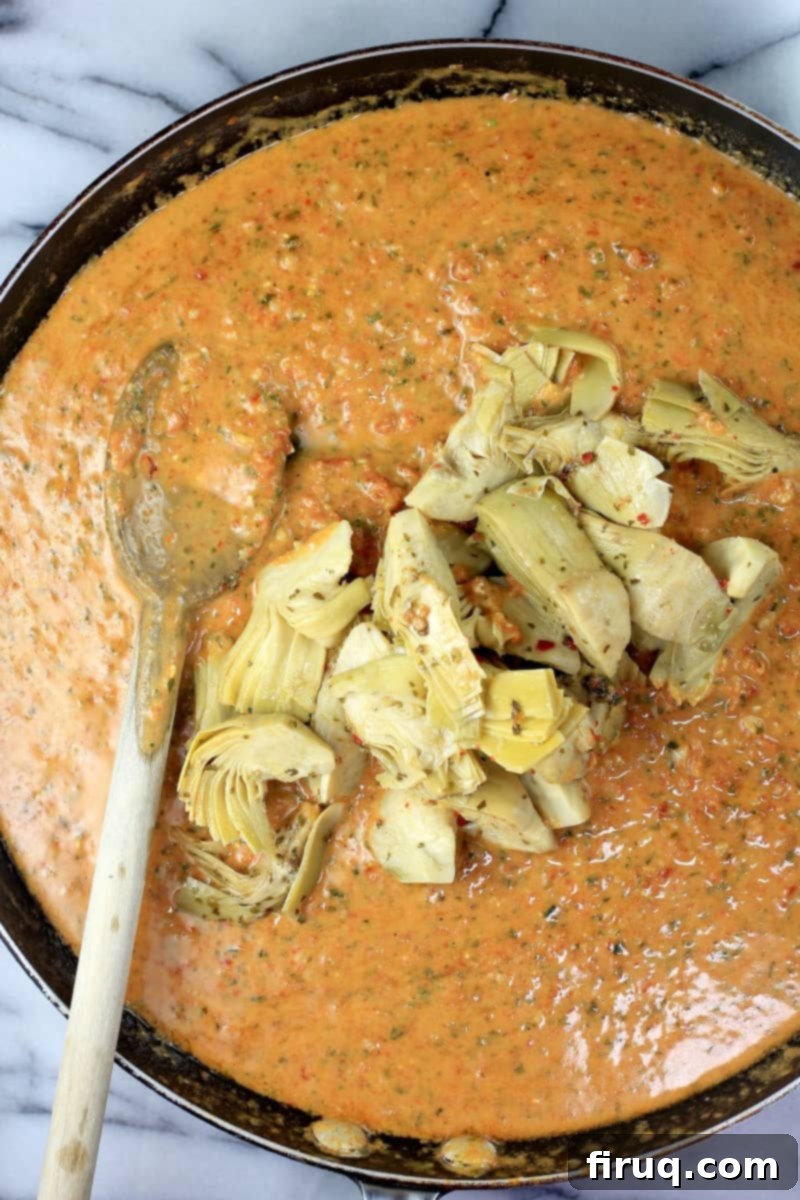 Rich Sun Dried Tomato Pesto Pasta 9 artichoke quarters piled on sun dried tomato pesto sauce in skillet with wooden spoon on the side