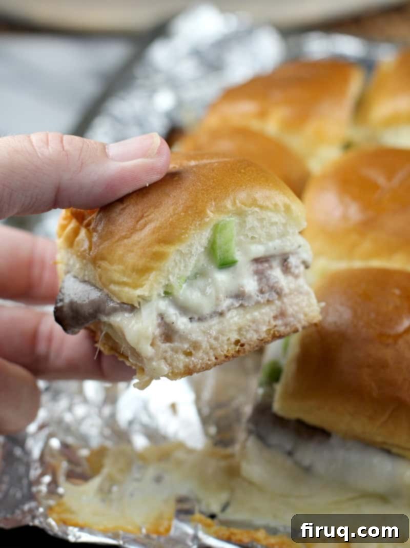 Grilled Philly Cheesesteak Bites 12 A hand reaching for a grilled Philly cheesesteak slider, with more delicious sliders visible in the background.