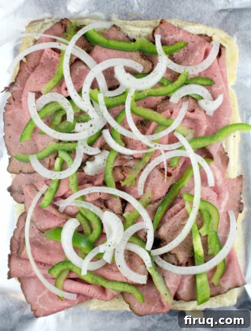 Grilled Philly Cheesesteak Bites 8 A top-down view of a half-assembled batch of Philly cheesesteak sliders, showing the organized layers of roast beef, thinly sliced onion, and green bell pepper on the sweet Hawaiian rolls.
