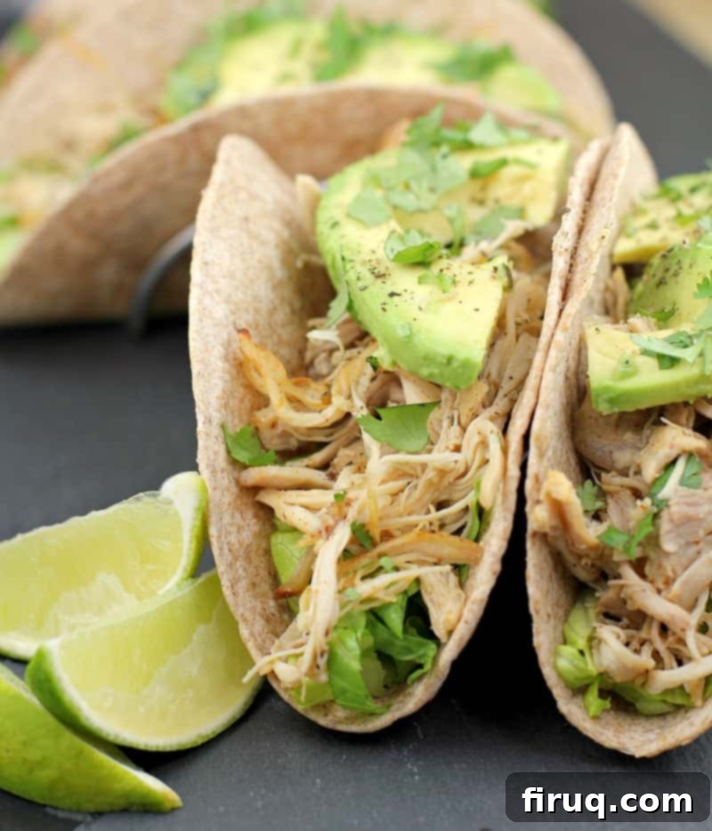 Instant Pot Chicken Carnitas 12 2 whole wheat tortillas stuffed with lettuce, chicken, and avocado on a slate with lime wedges