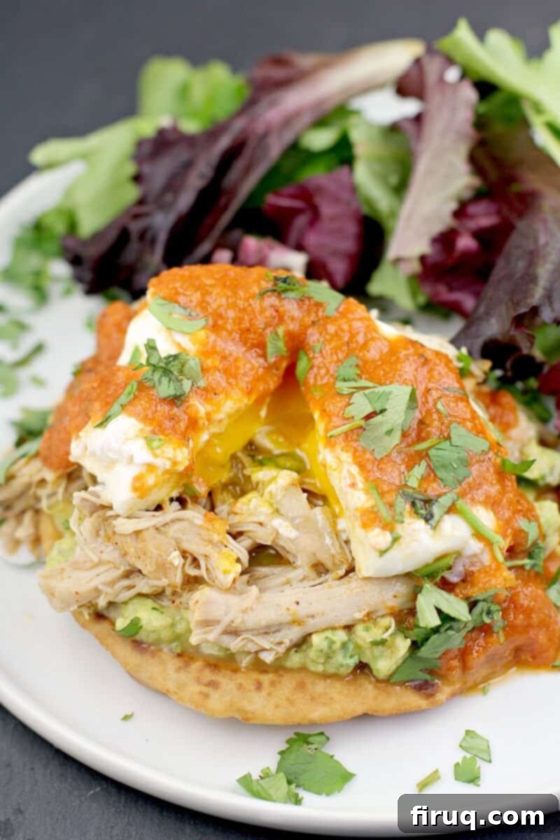 Huevos Rancheros Benedict 2 Mexican style Eggs Benedict on a serving plate with a side salad; a poached egg on top is split to show the runny yolk