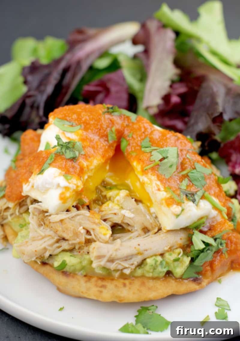 Huevos Rancheros Benedict 12 assembled mexican eggs benedict on a white plate with side salad; poached egg on top is split to show runny yolk