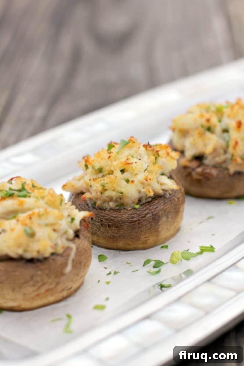 Crab-Filled Mushroom Caps 2 three crab stuffed mushrooms on a piece of white parchment on a silver serving plate