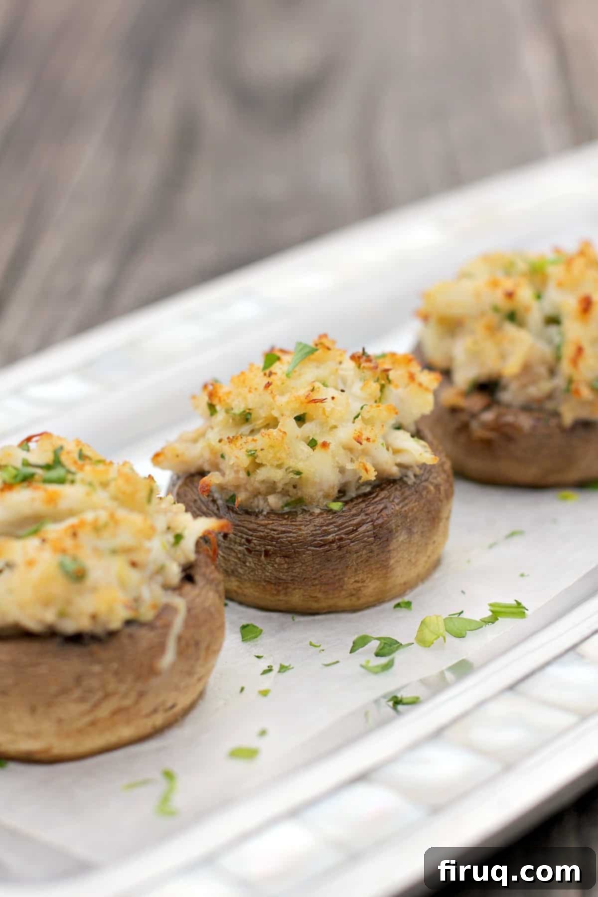Crab-Filled Mushroom Caps 12 three crab stuffed mushrooms on a piece of white parchment on a silver serving plate