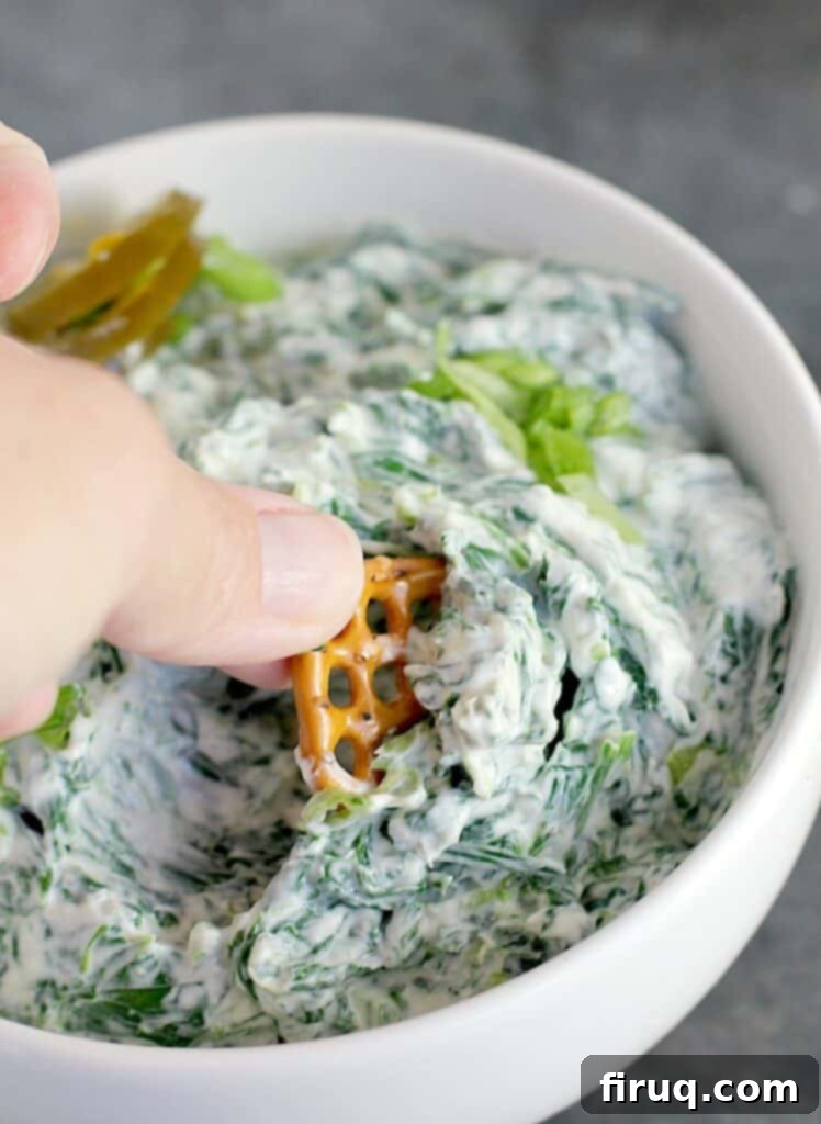 Warm Green Chili Artichoke Dip 8 hand scooping a pretzel into spinach dip