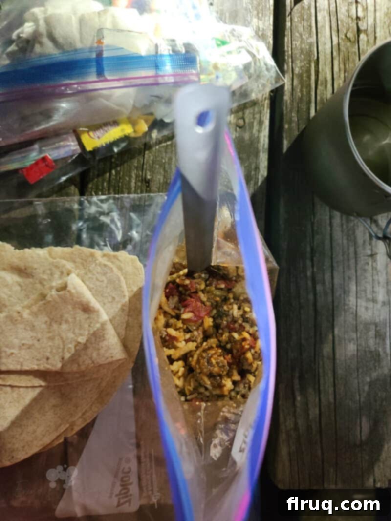 Adventure Sloppy Joes 12 picnic table surface with tortilla and ziploc bag with backcountry sloppy joes and spoon; metal mug off to the side
