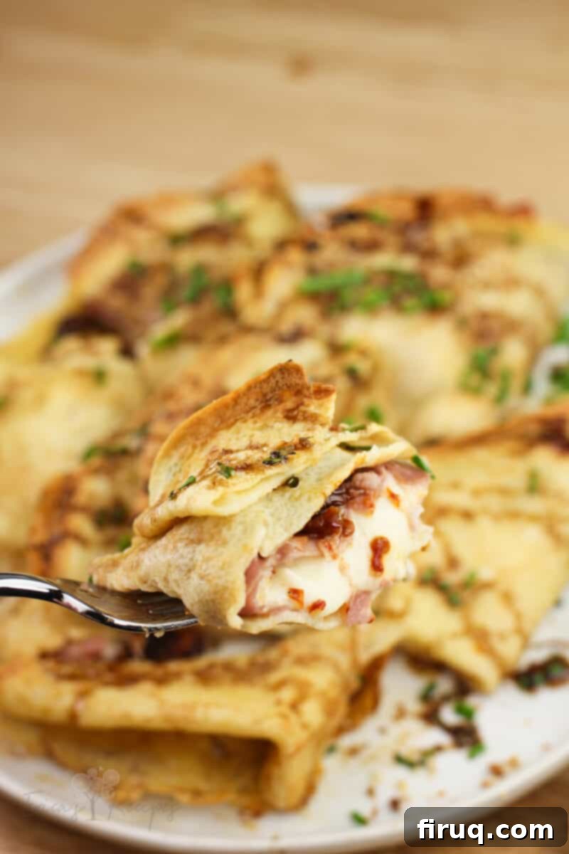 Prosciutto and Cheese Crepes 3 fork holding piece of crepe showing sun-dried tomato, prosciutto, and mozzarella filling