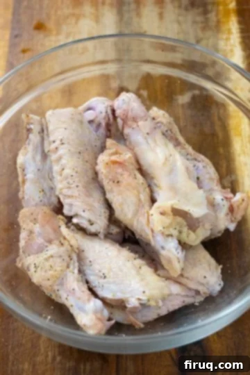 Crispy Air Fryer Garlic Parmesan Wings 4 Seasoning raw chicken wings with a blend of garlic powder, onion powder, salt, and pepper in a large mixing bowl