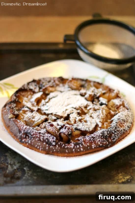 German Apple Pancake Slice A slice of German Apple Pancake, beautifully golden and topped with a dusting of powdered sugar, served on a pristine white plate.