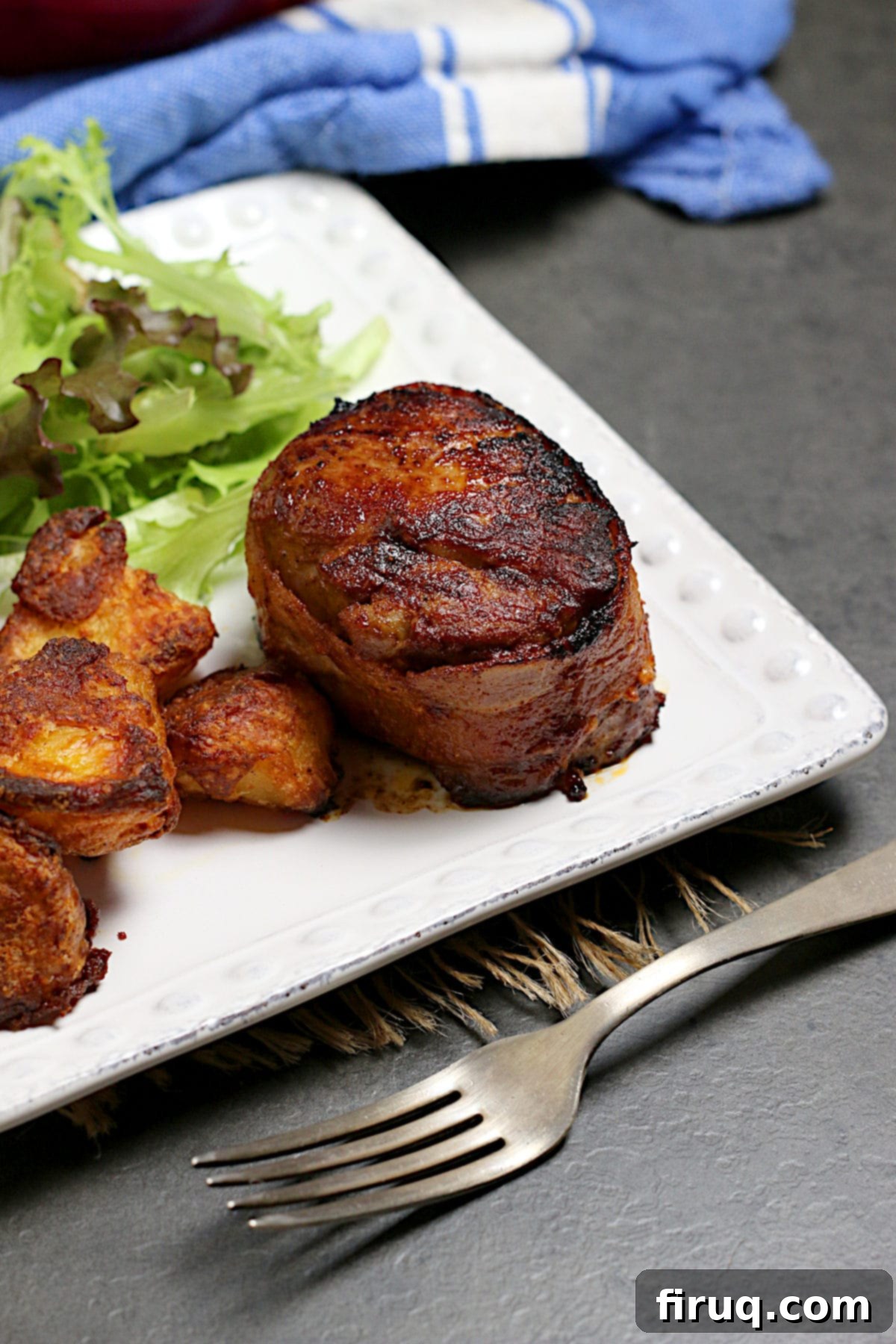 Finished Bacon Wrapped Pork Medallion with Sides Bacon Wrapped Pork Medallion served on a white plate with roasted potatoes and a fresh green salad.