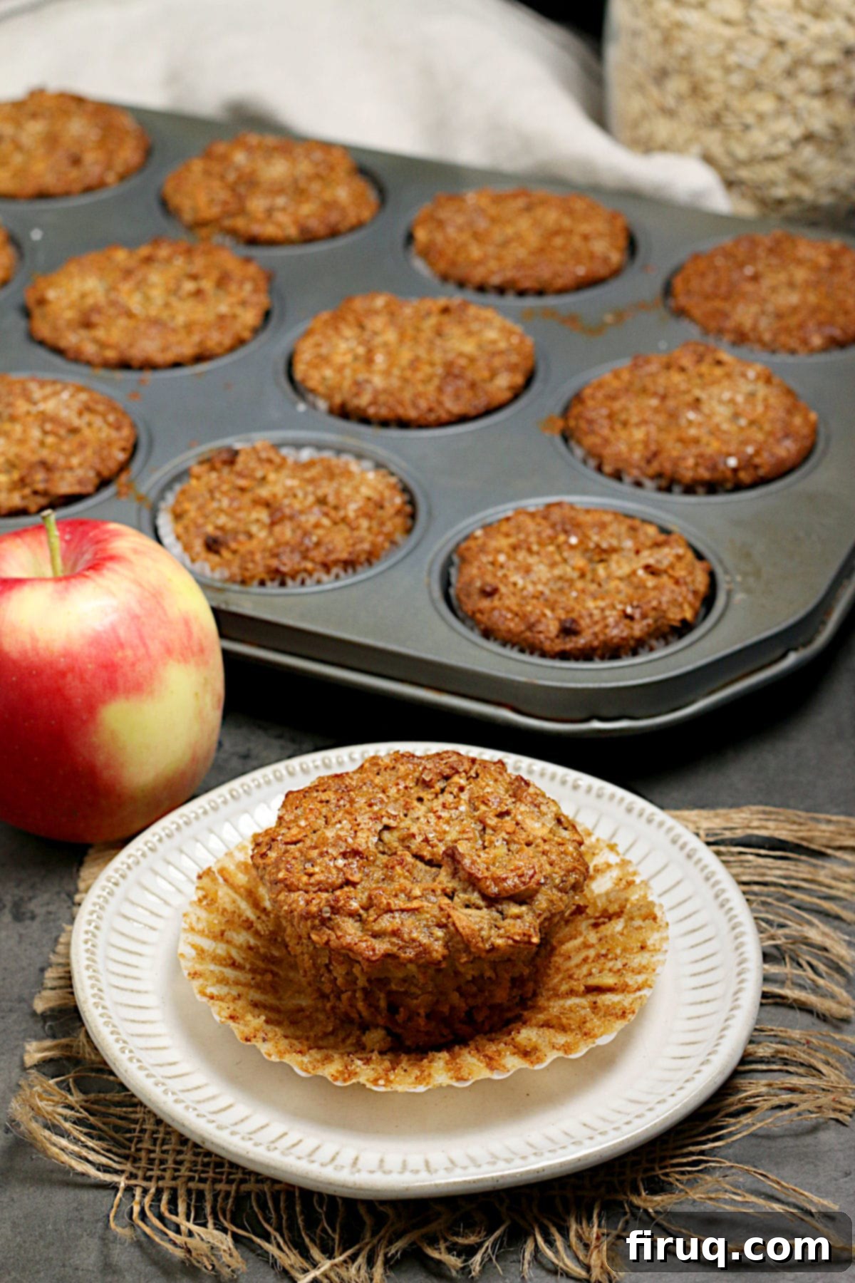 Unwrapped Apple Cinnamon Oatmeal Muffin Detail An unwrapped Apple Cinnamon Oatmeal Muffin on a small white plate, showing its tender interior and visible texture. Perfect for a healthy snack.