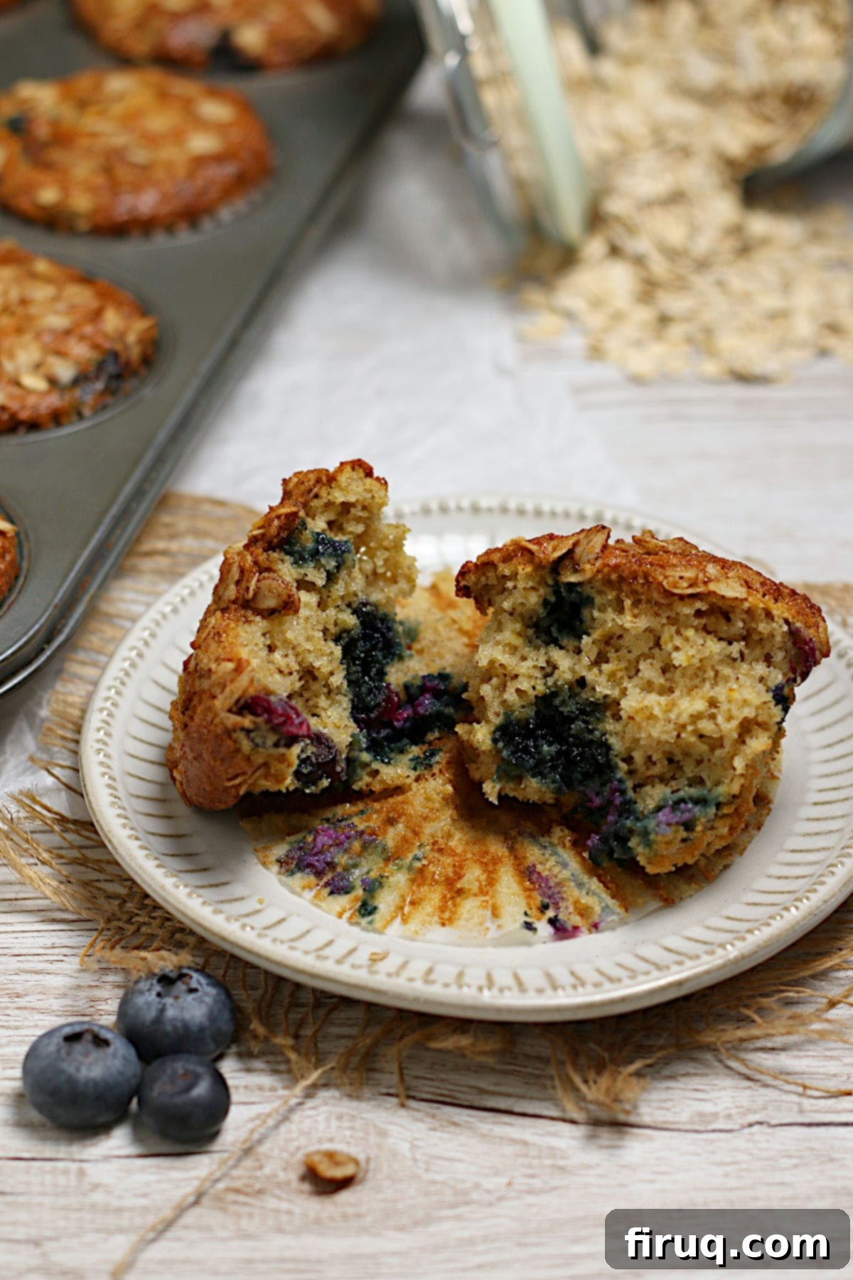 Delicious Blueberry Oatmeal Muffins A blueberry oatmeal muffin broken into two pieces on a small white plate, highlighting its tender crumb and plump blueberries throughout.