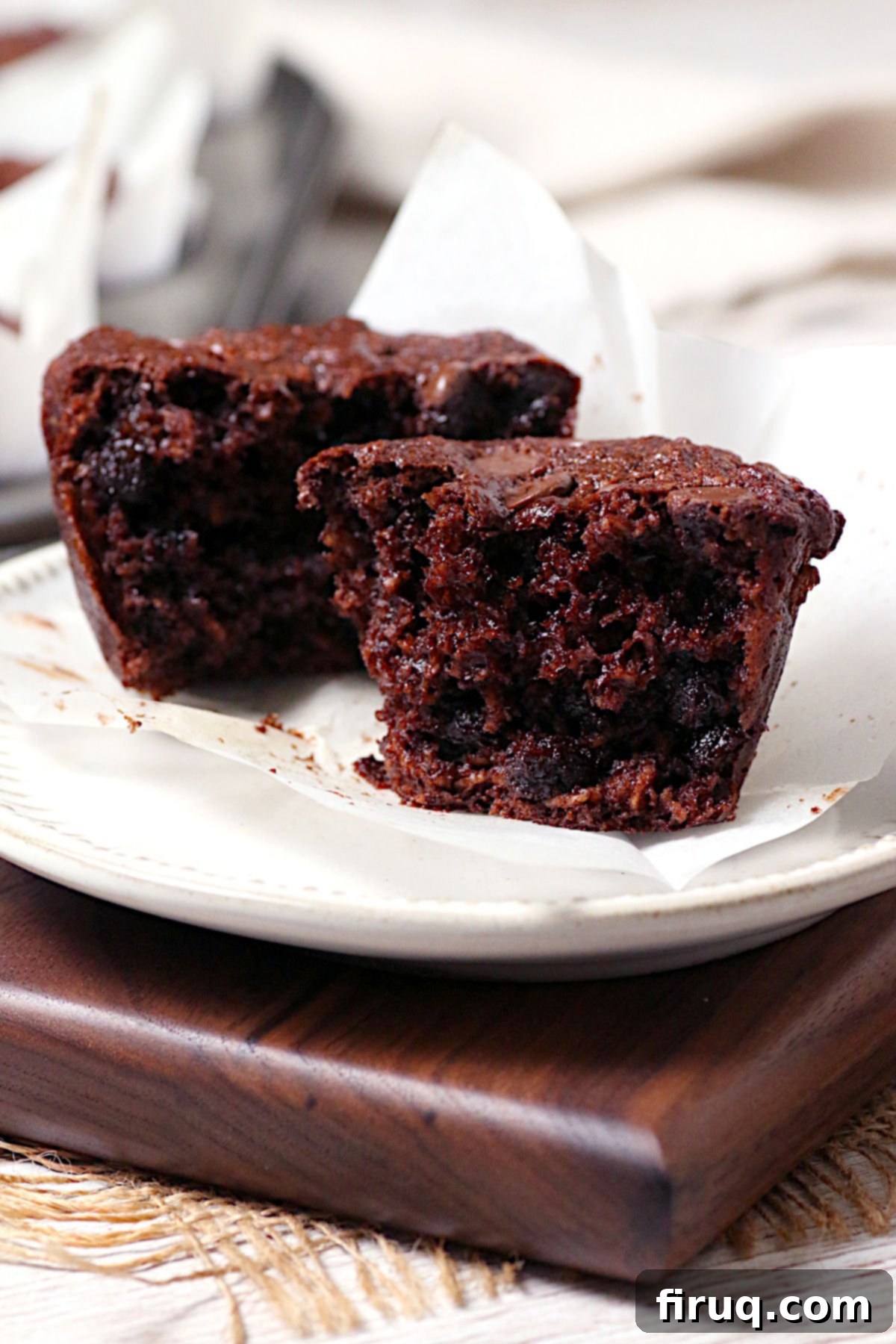 Rich Flourless Double Chocolate Oatmeal Muffins Two halves of a double chocolate oatmeal muffin on a white plate, showing rich chocolate chunks and a moist, dark interior.