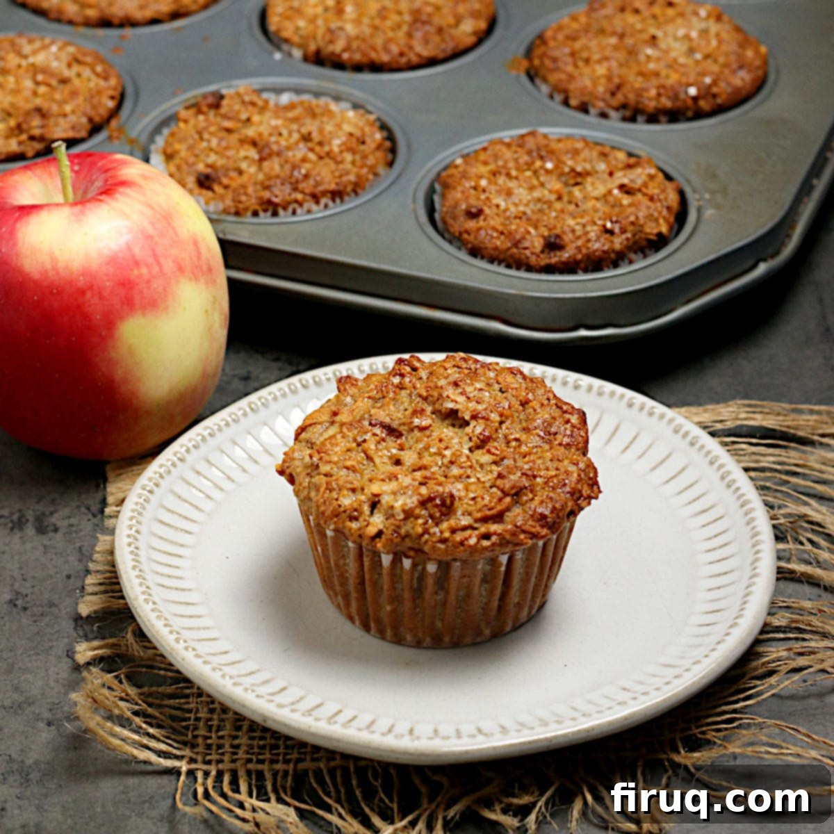 Apple Cinnamon Oatmeal Muffins An apple cinnamon oatmeal muffin on a small white plate, ready to be eaten. A delicious and healthy snack or breakfast item.