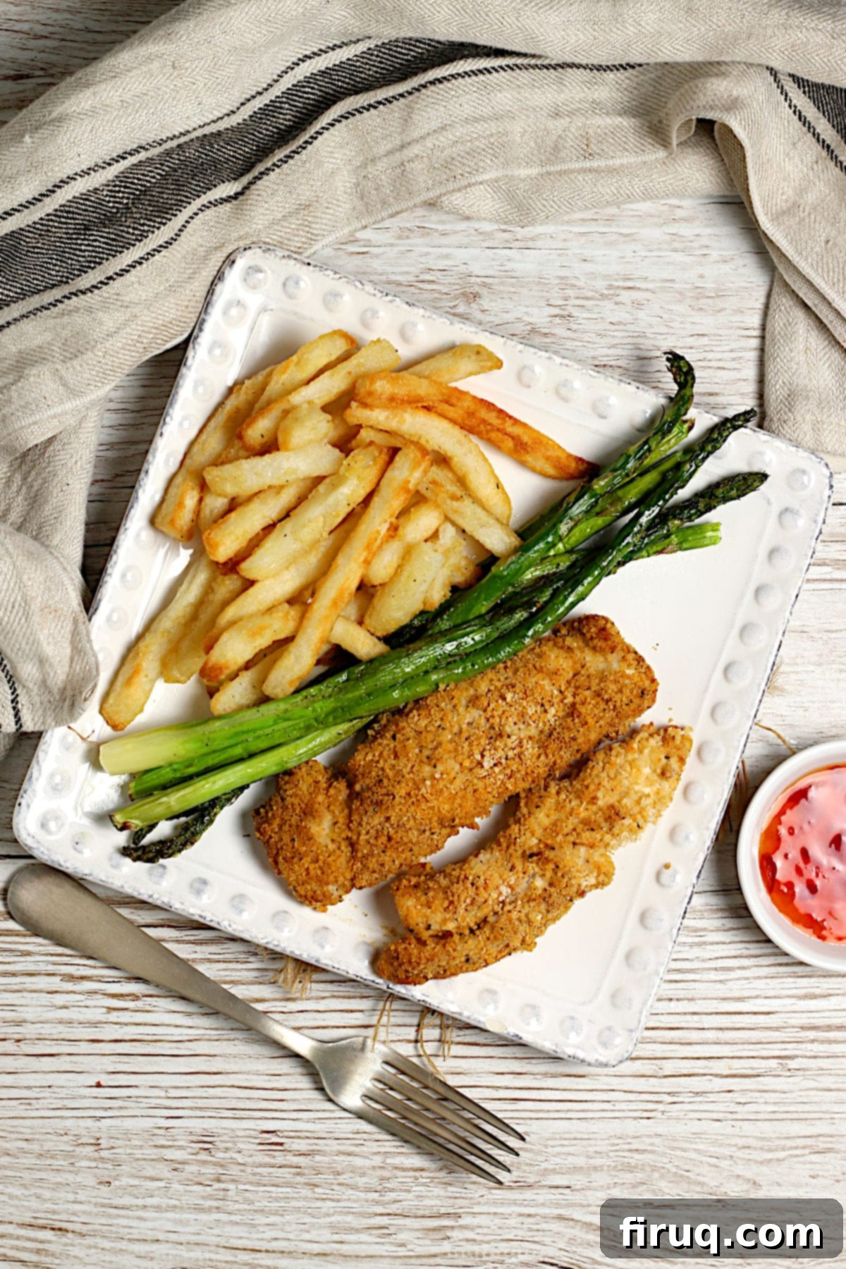Oven-Baked Chicken Fingers with Sides Overhead photo of a square dinner plate containing oven-baked chicken fingers, roasted asparagus, and french fries.