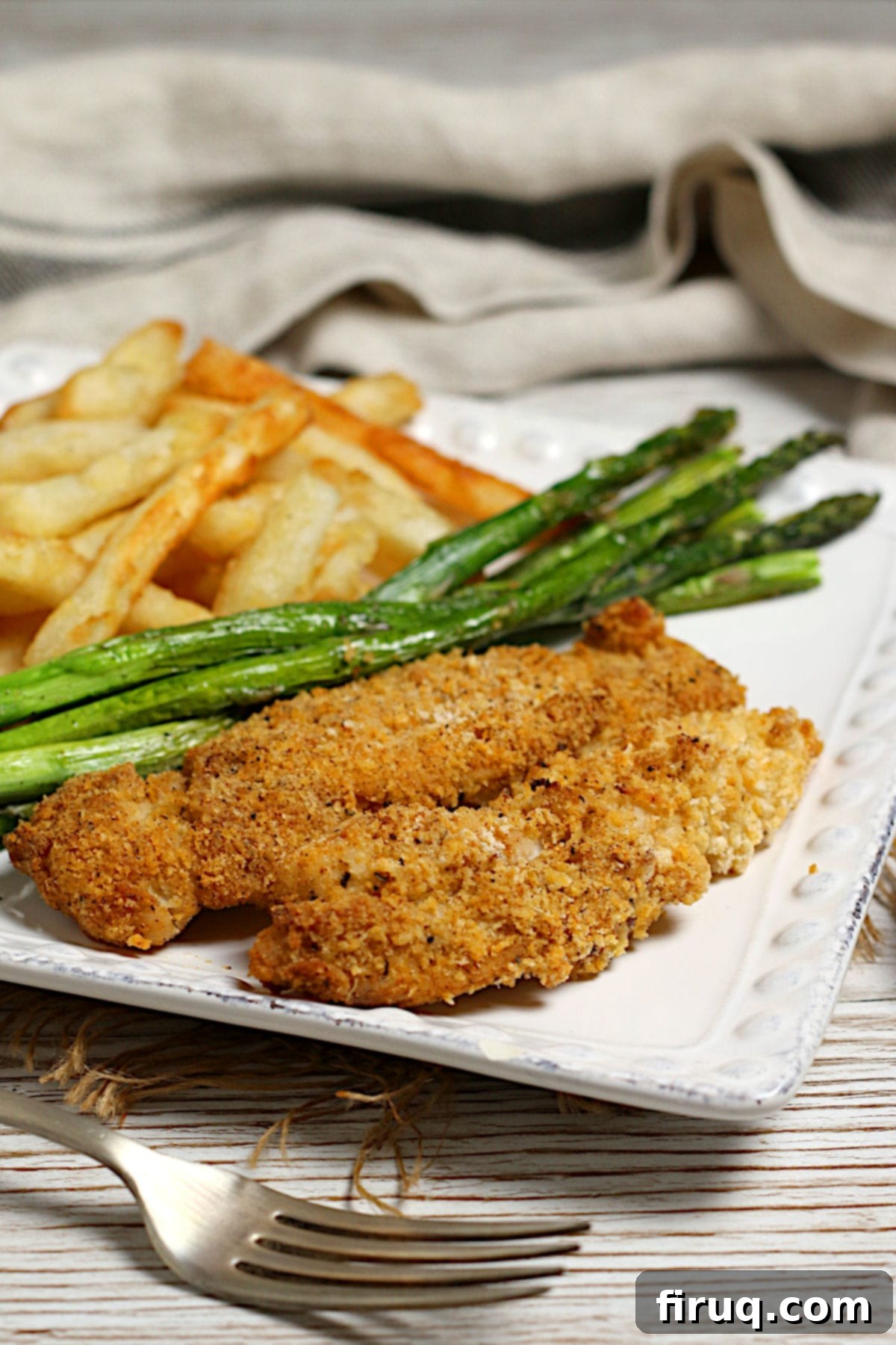 Close-up of Crispy Chicken Tenders A close-up photo of oven-baked chicken tenders on a dinner plate with roasted asparagus and french fries.