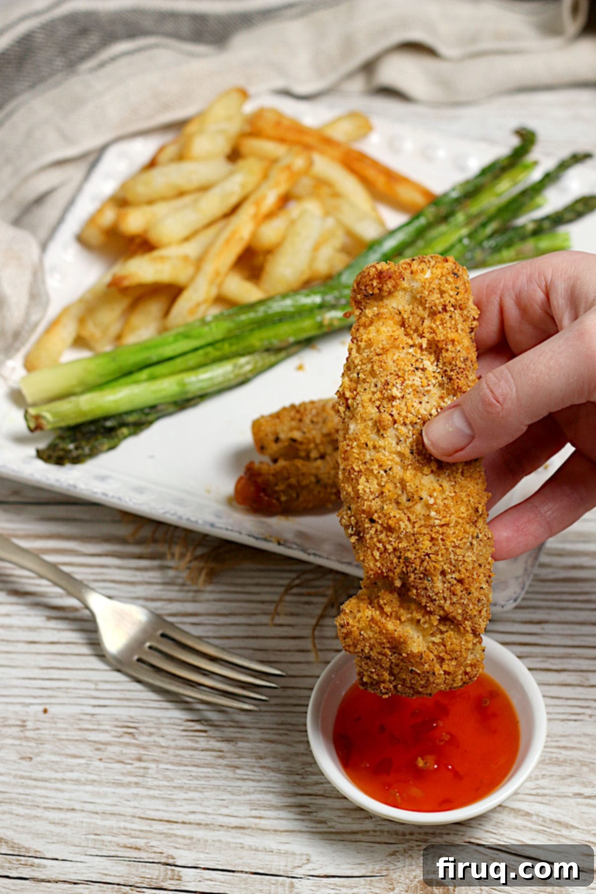 Chicken Tender with Sweet Chili Sauce A hand holding an oven-baked chicken tender over a small bowl of Thai sweet chili sauce.