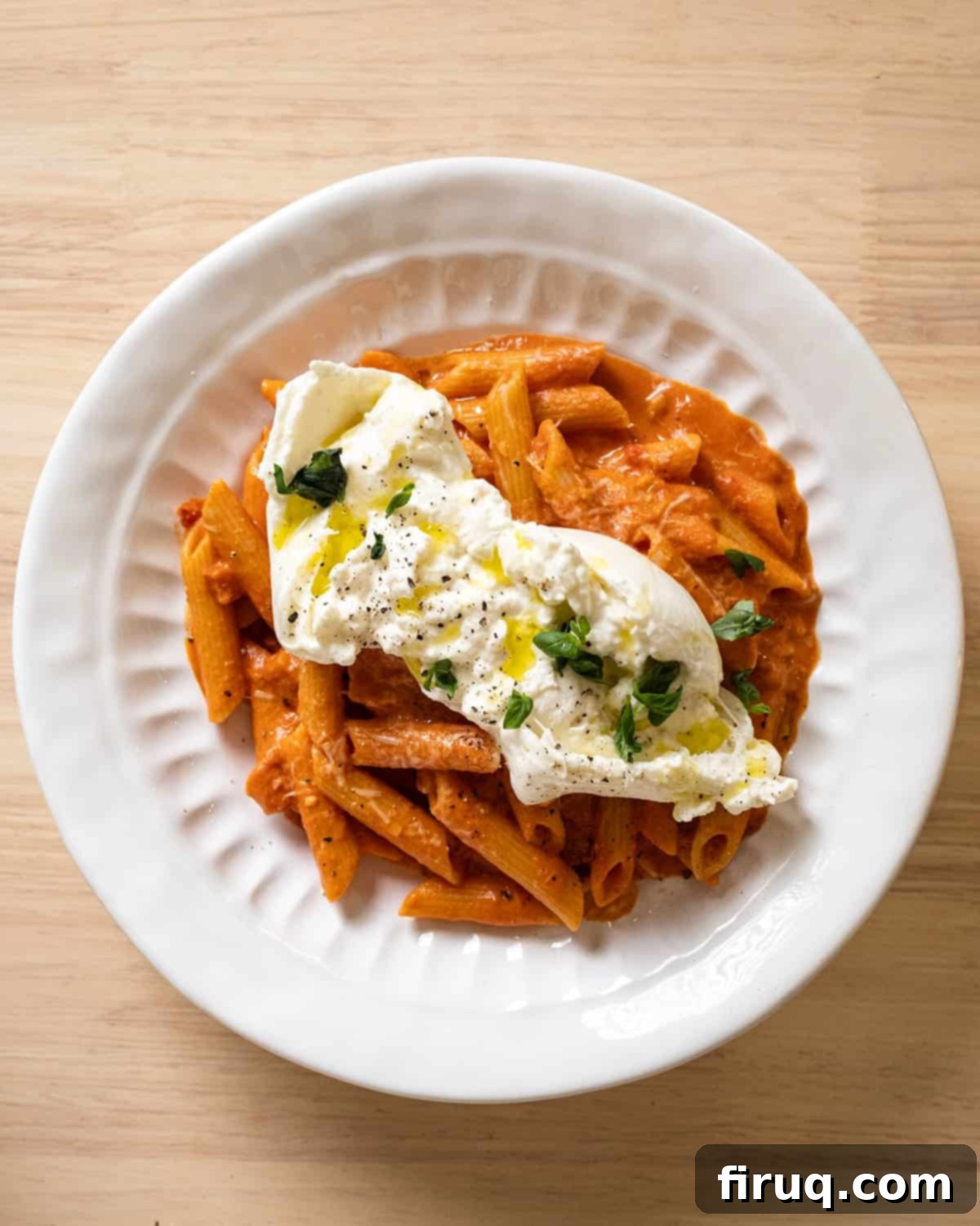 Fiery Vodka Sauce 9 A bowl of penne a la vodka with a generous dollop of creamy burrata melting on top, garnished with fresh basil.