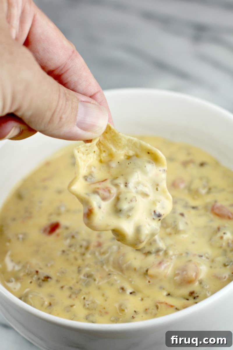Irresistible Velveeta Rotel Sausage Dip 3 Hand holding a scoop tortilla chip with queso over a bowl full of queso