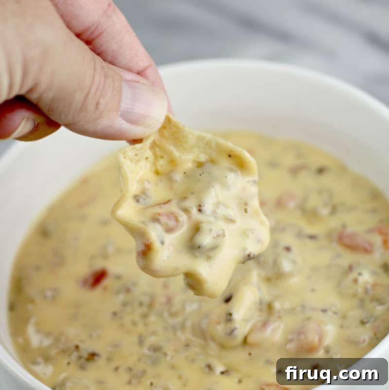 Irresistible Velveeta Rotel Sausage Dip 8 Close view of hand holding a scoop tortilla chip with queso over a bowl full of queso