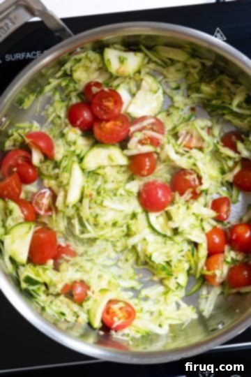 Sun-Kissed Zucchini Pasta 5 Grated zucchini and halved cherry tomatoes being stirred into fragrant olive oil and garlic in a pan, beginning to form the sauce base.