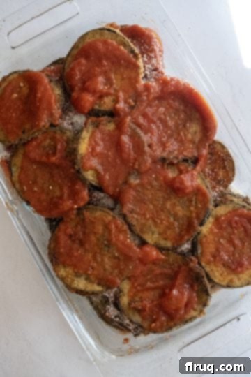The Ultimate Homemade Eggplant Parmigiana 8 The initial layer of sauce and fried eggplant in a baking dish.