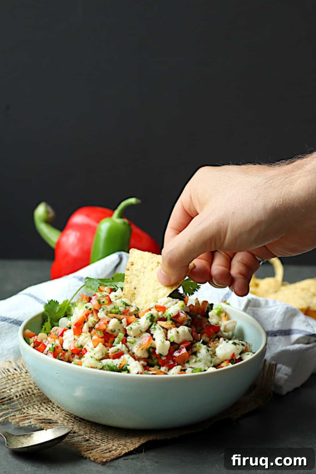 Ceviche A hand reaching to dip a tortilla chip into a vibrant bowl of fresh ceviche.