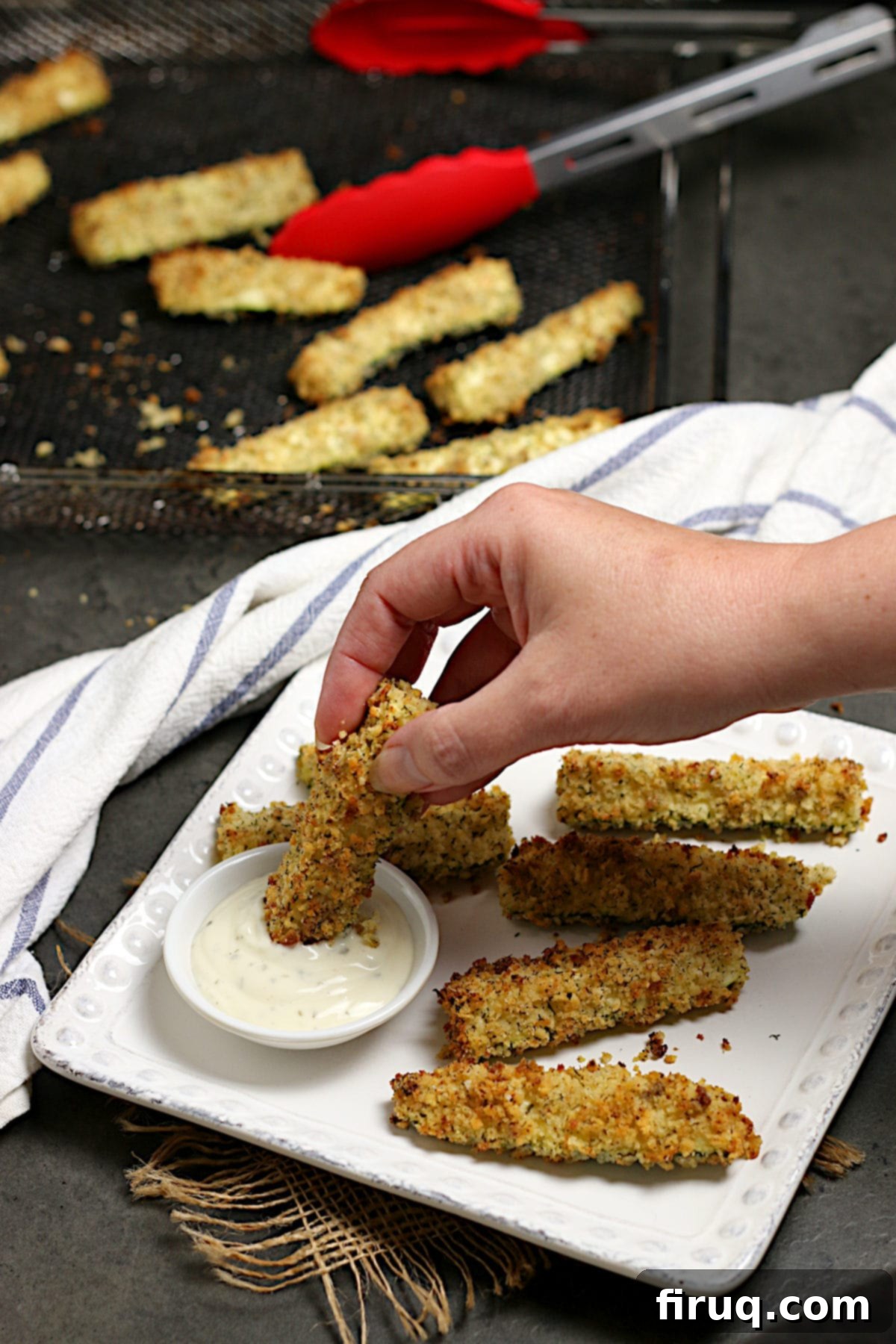 Dipping Air-Fried Zucchini Sticks A hand gracefully dipping a golden-brown air-fried zucchini stick into a creamy ranch dip, highlighting its crispy coating.