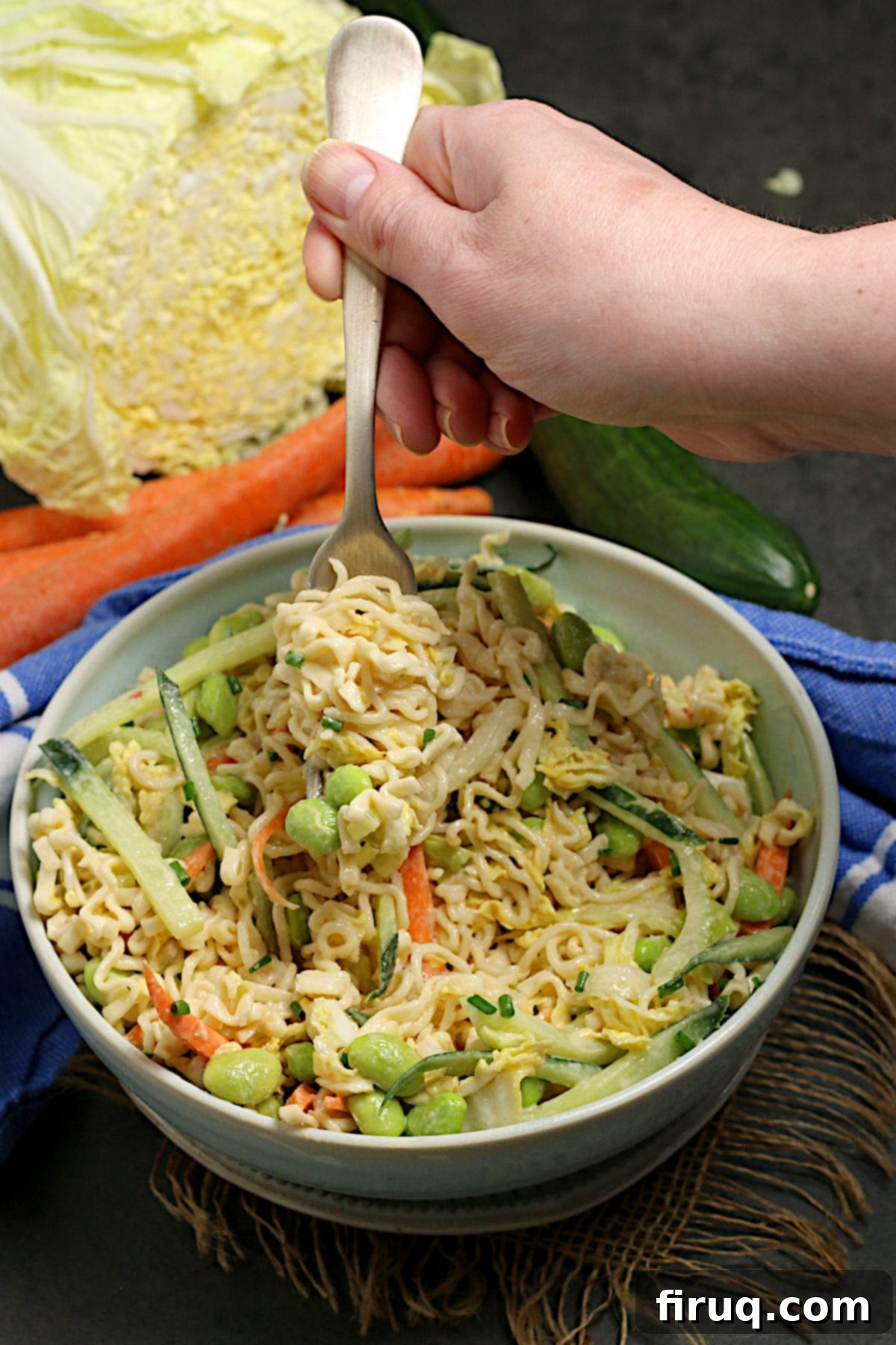 Noodle Salad with Tahini Dressing A hand scooping a forkful of Noodle Salad with Tahini Dressing from a pale blue bowl.