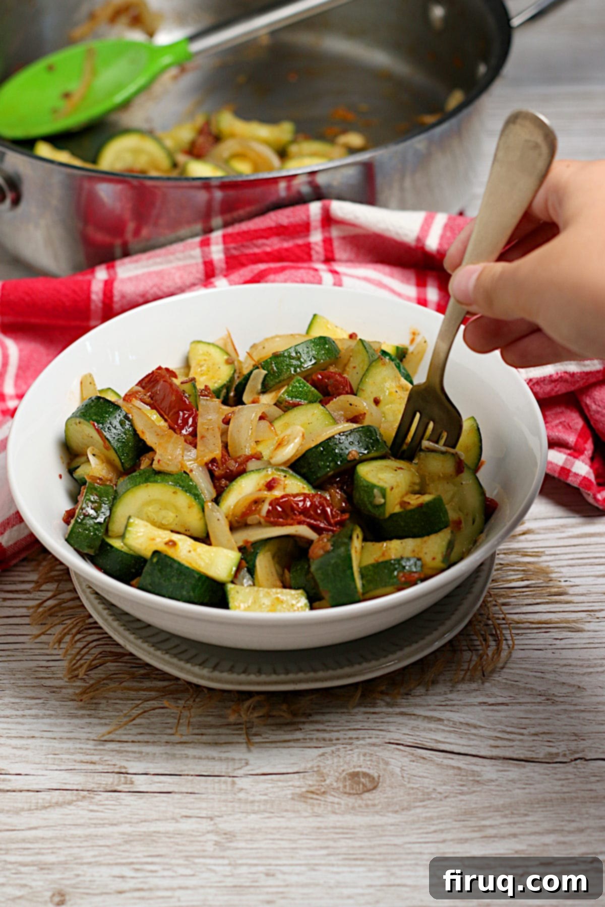 Serving Zucchini with Sun-Dried Tomatoes and Onions A fork scooping Zucchini with Sun-Dried Tomatoes and Onions from a white bowl.