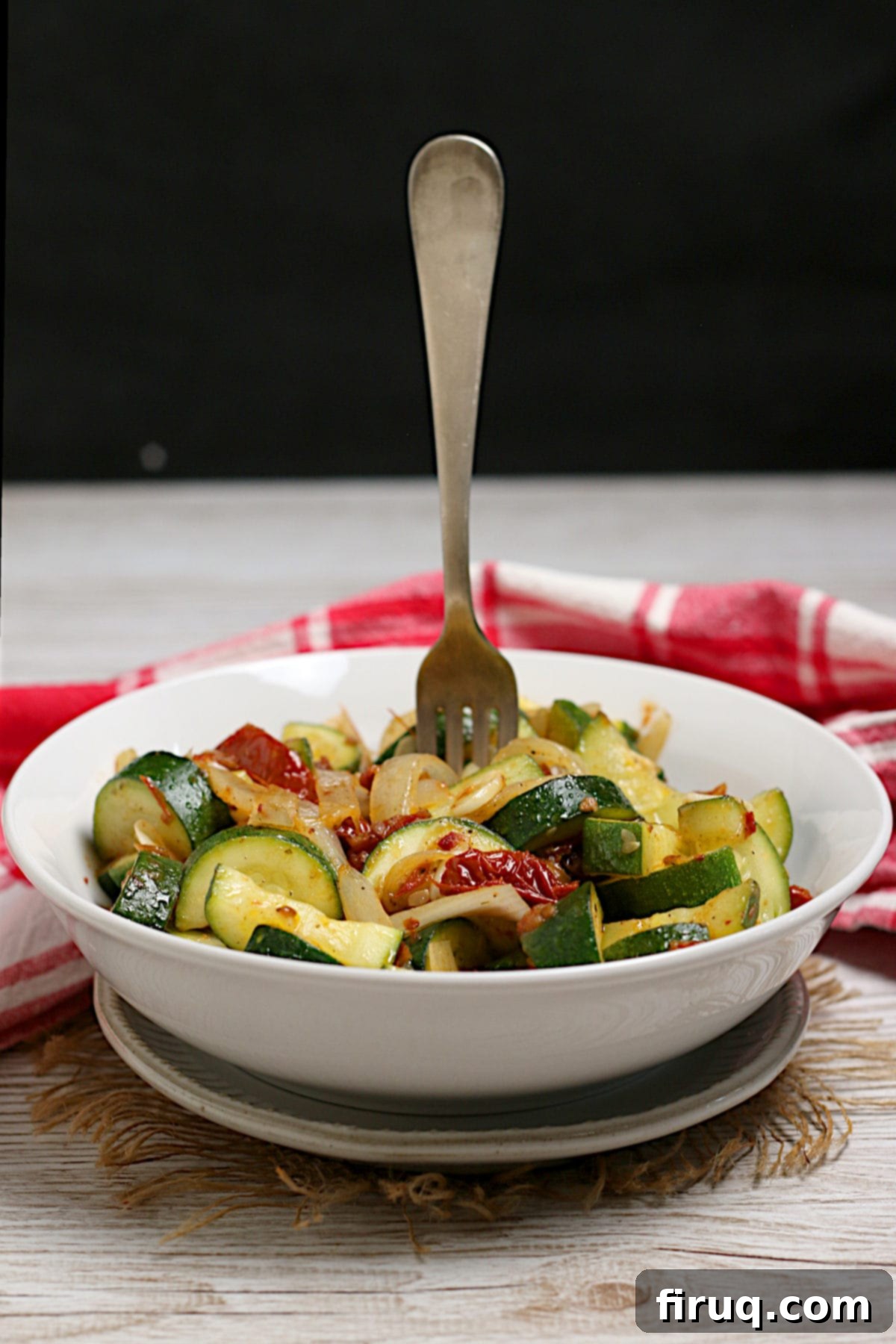 Zucchini Side Dish Ready to Enjoy A fork standing upright in a bowl of Zucchini with Sun-Dried Tomatoes and Onions.