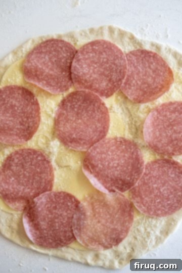 Savory Pepperoni Spiral 4 Salami slices layered on top of cheese on pizza dough, ready for the next layer of pepperoni.