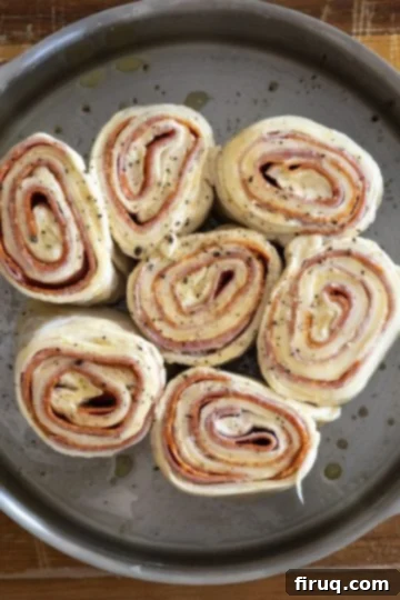 Savory Pepperoni Spiral 6 Sliced pepperoni stromboli rolls arranged in a round baking pan with space around the edges, ready for baking.