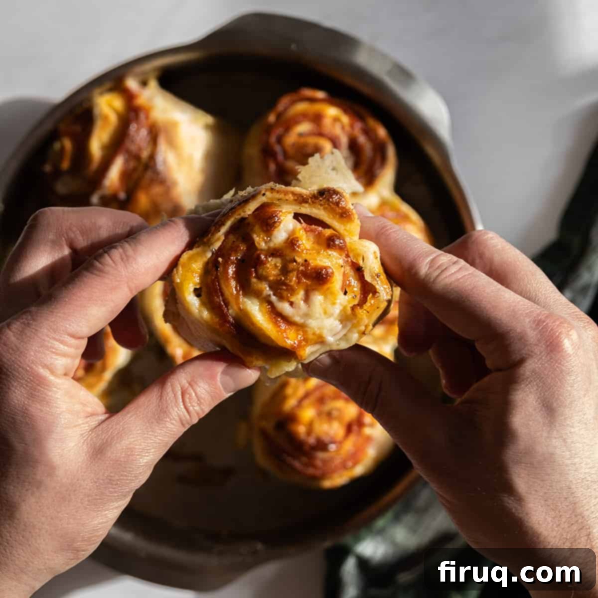 Savory Pepperoni Spiral 8 A hand holding a slice of freshly baked pepperoni stromboli, showing the melted cheese and pepperoni inside.