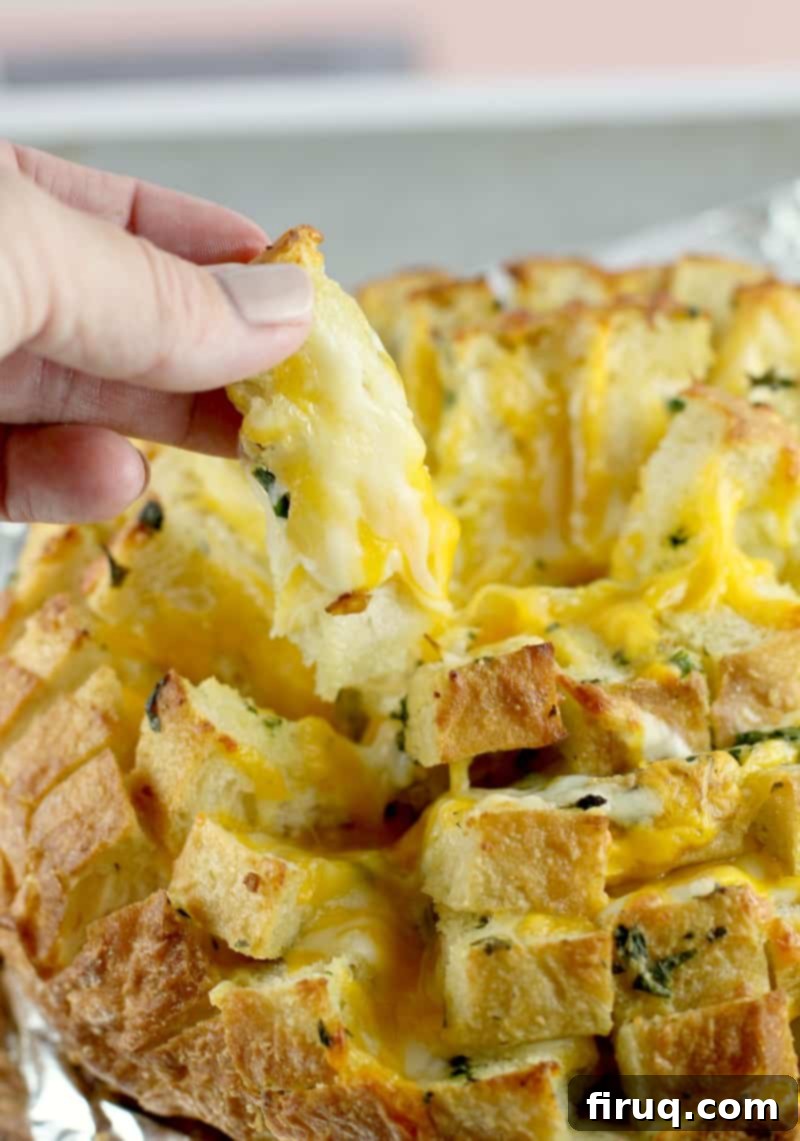 Loaded Cheesy Garlic Bread 2 Side view of a hand lifting up a piece of the garlic herb and cheese pull-apart bread to show the cheesiness, with strands of melted cheese stretching out.