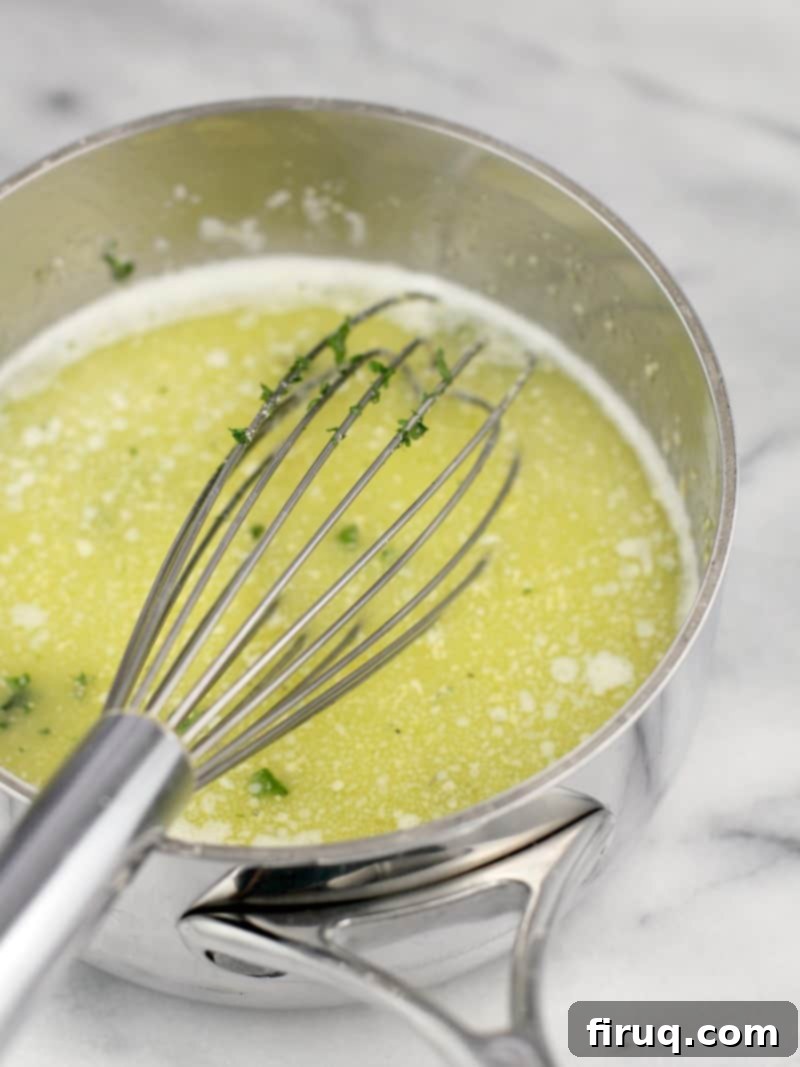 Loaded Cheesy Garlic Bread 5 A small steel saucepan with a whisk on a marble countertop, containing the melted butter and garlic mixture.