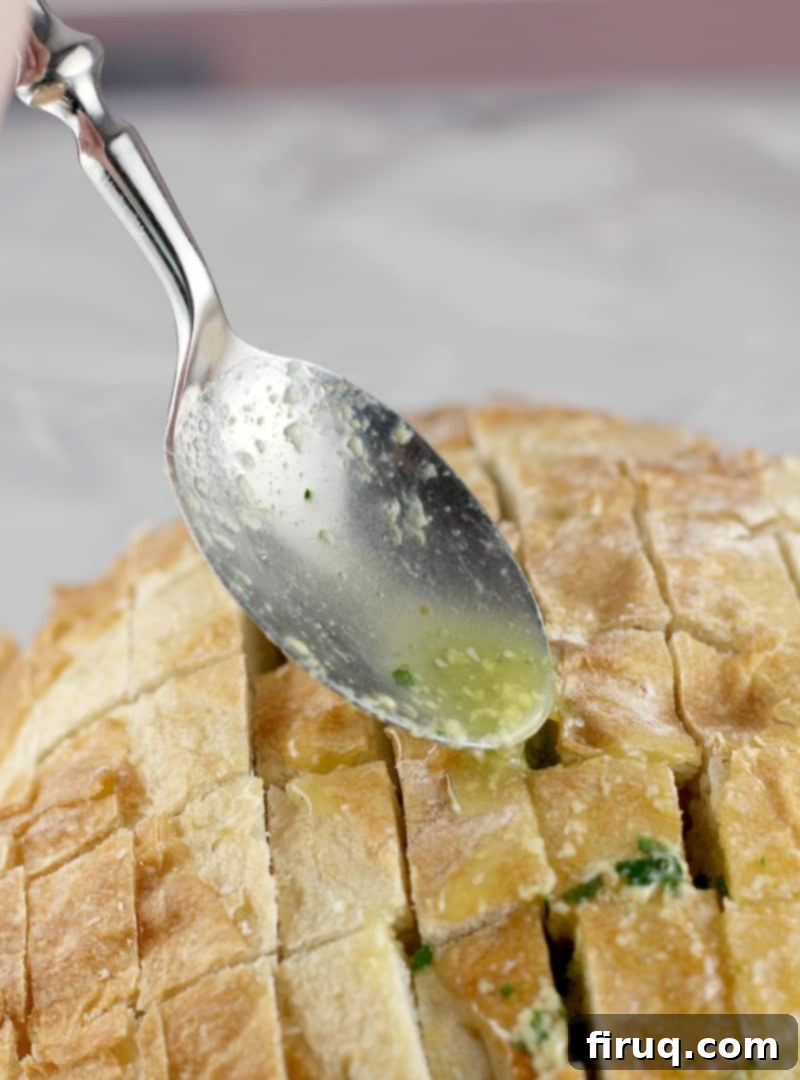 Loaded Cheesy Garlic Bread 6 A spoon drizzling the butter herb mixture into the cross-hatched cuts on the bread loaf, preparing it for stuffing.