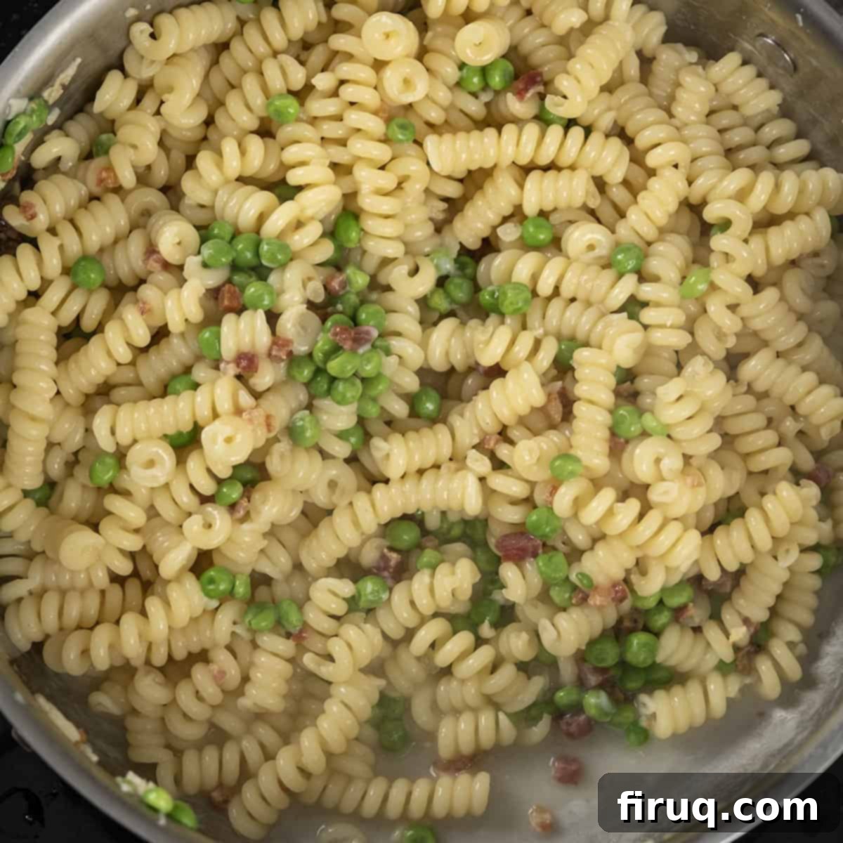 Pea and Pancetta Pasta 7 Cooked fusilli pasta being combined with peas, garlic, and pancetta fat in a large pan.