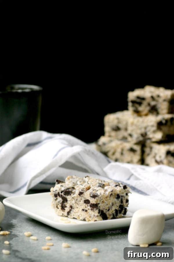 Single Oreo Rice Krispie Treat Close-up of a single Cookies and Cream Rice Krispie Square resting on a white plate, highlighting the visible Oreo chunks and the sticky, sweet texture.