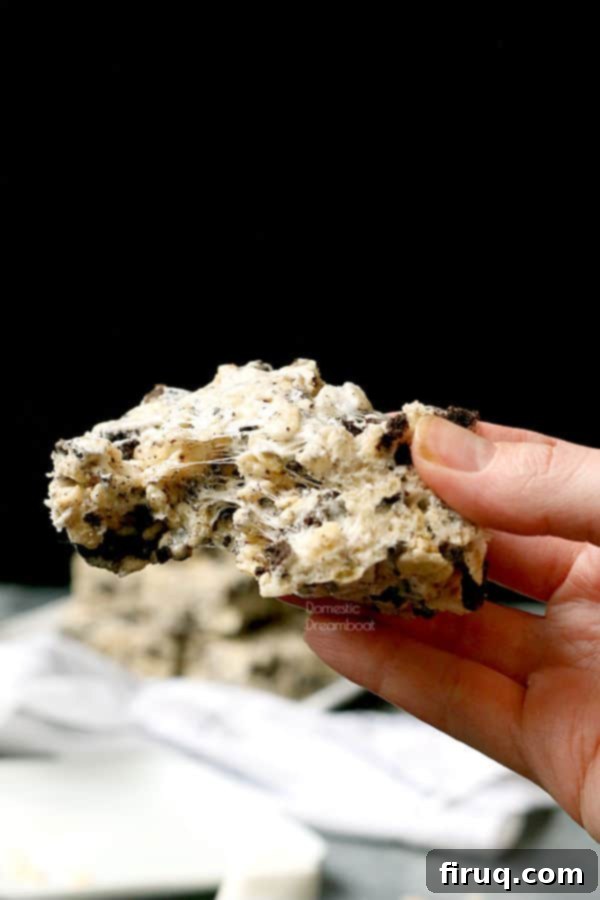 Hand Holding Oreo Rice Krispie Treat A hand presenting a freshly made Cookies and Cream Rice Krispie Square, with a bite taken out, showing the gooey interior.
