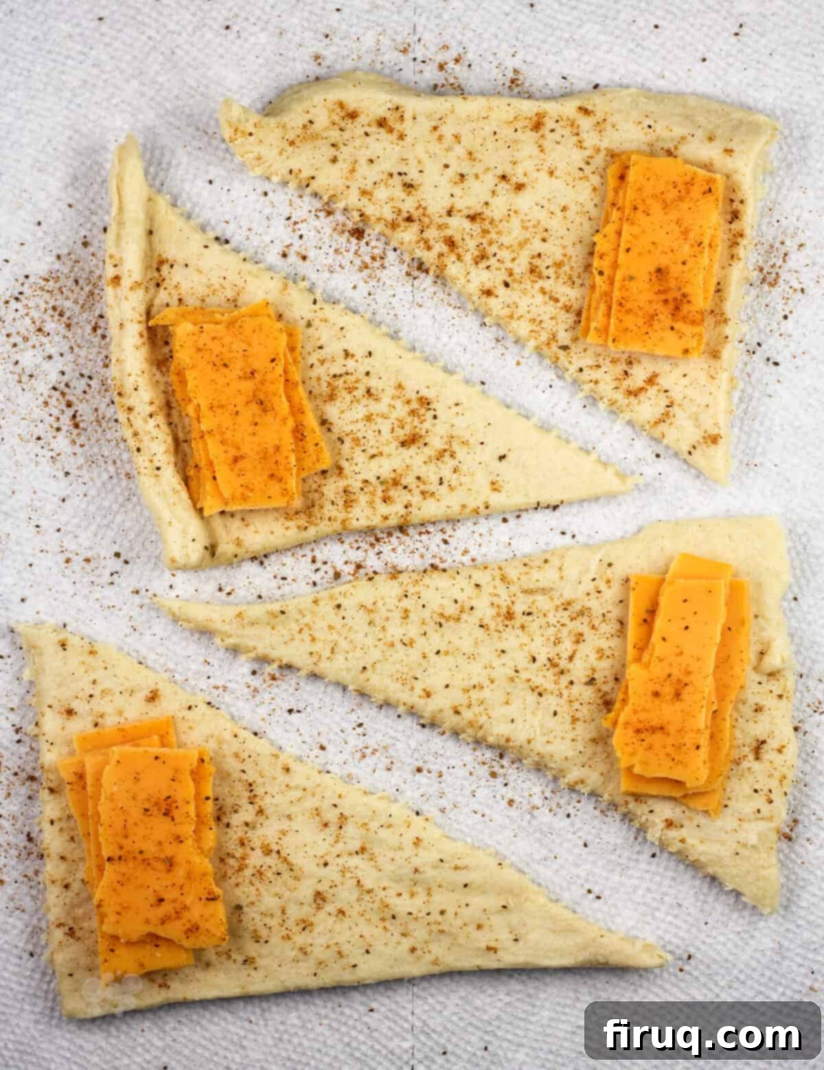 Melted Cheddar Crescent Rolls 4 Crescent dough triangles laid out with sharp cheddar cheese and a sprinkle of Old Bay seasoning, ready for rolling.
