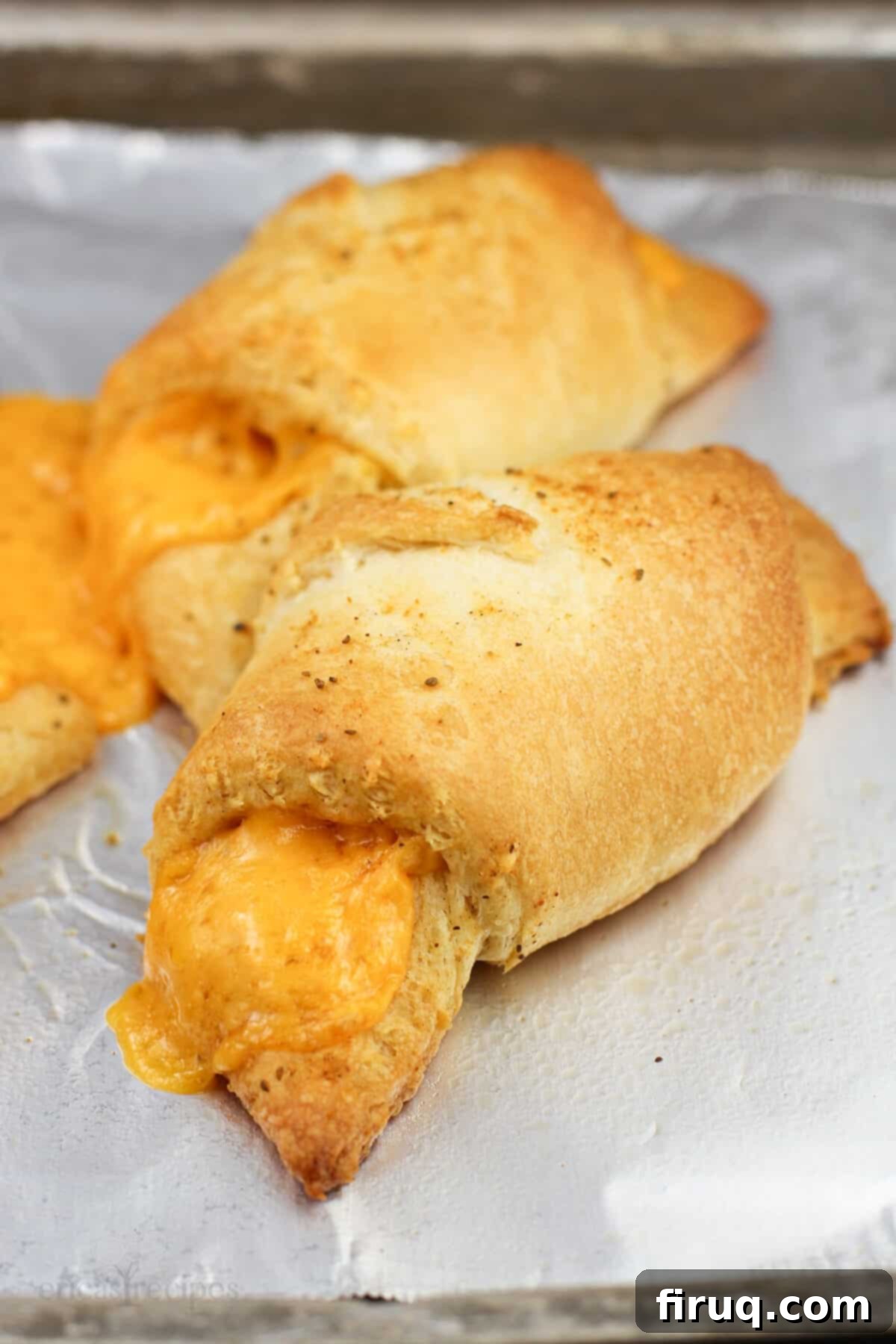 Melted Cheddar Crescent Rolls 6 Baked cheddar cheese stuffed crescent rolls on a baking sheet, golden and ready to serve.
