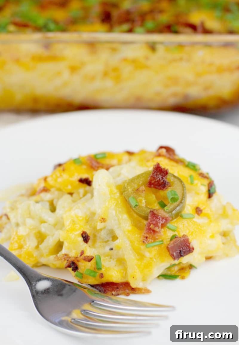 Kickin' Hash Brown Popper Casserole 2 Plated serving of creamy and cheesy hash brown casserole with bacon and jalapenos on a white plate with a fork, ready to eat.