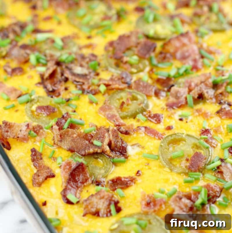 Kickin' Hash Brown Popper Casserole 3 Close-up view of a baked hash brown casserole in a baking dish, generously topped with melted cheese, crispy bacon bits, and sliced pickled jalapenos.